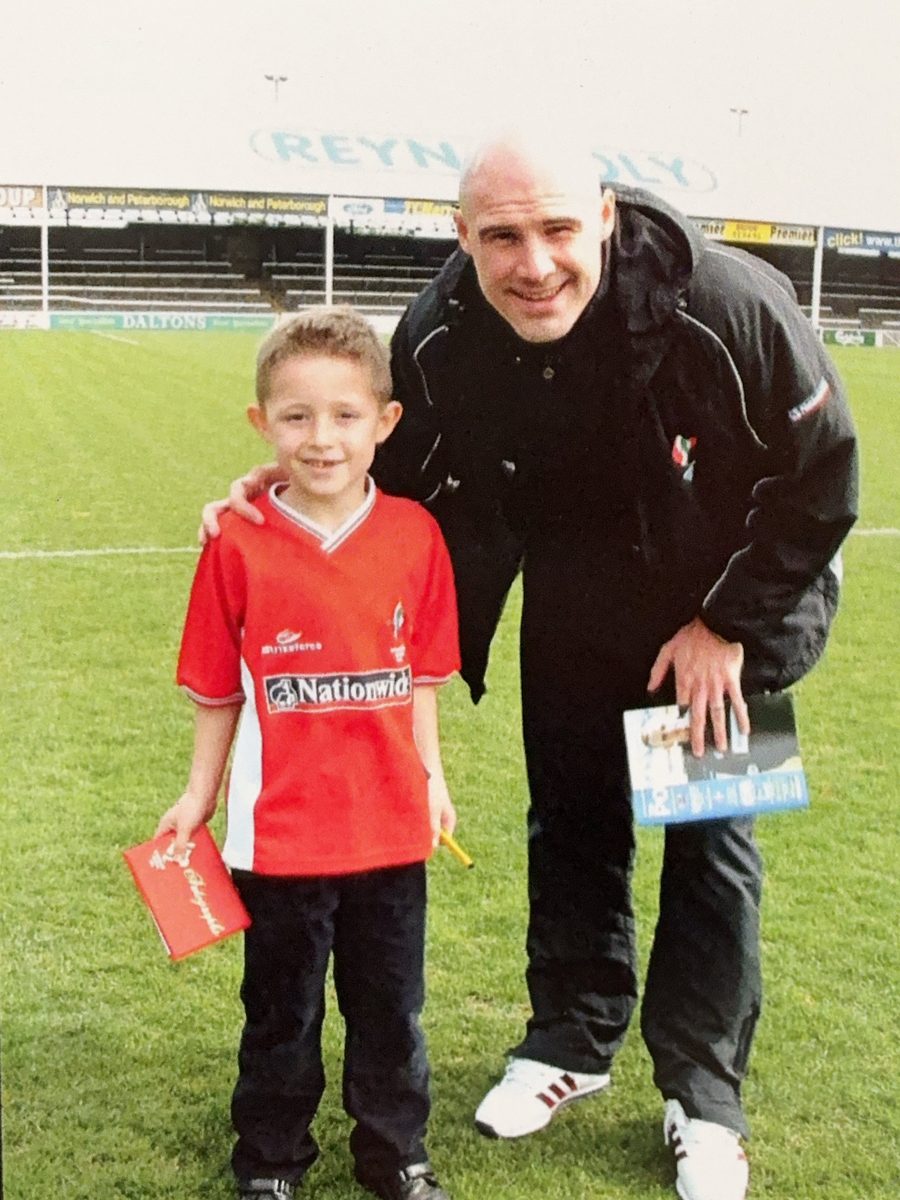 A young Jake Brown, now founder of Mindframe Performance, as a Swindon Town mascot on the pitch with a player in the early 2000s