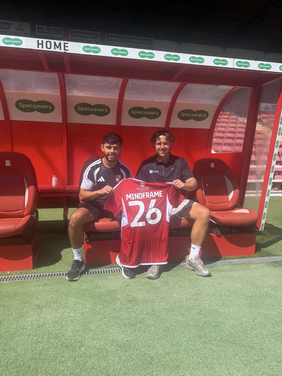 Jake Brown and Adam Labelle in the Swindon Town home dugout with a Mindframe shirt, marking the club's sport psychology partnership